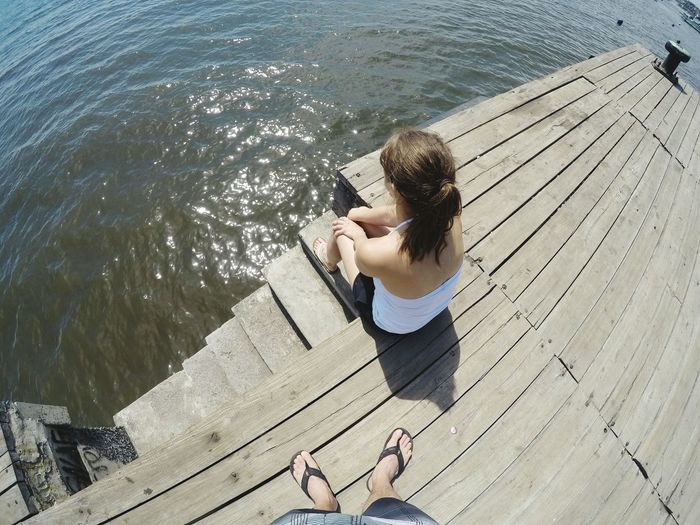 Low section of man with female friend on pier by sea during sunny day