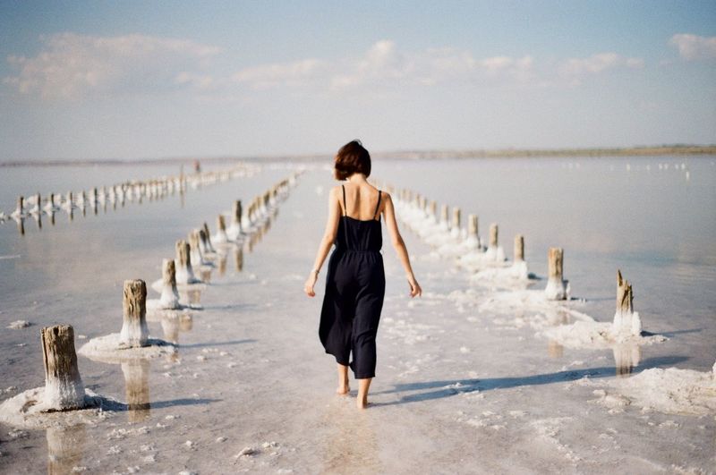 Rear view of woman walking on beach against sky