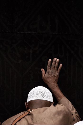 Rear view of muslim man touching kaaba while praying at al-haram mosque