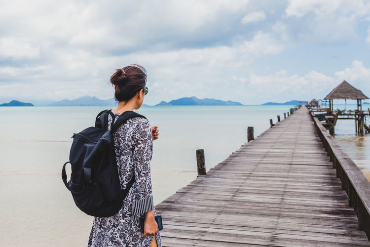 Rear view of woman standing on pier over sea against sky