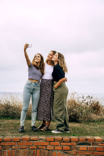 Cheerful smiling women hugging and taking selfie on mobile phone standing in countryside