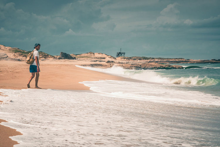 Rear view of man on shore at beach against sky