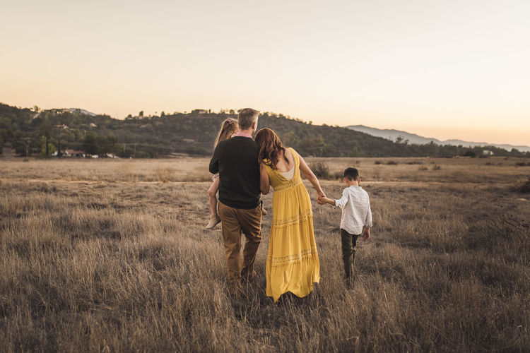 Young family holding hands while walking away in california field
