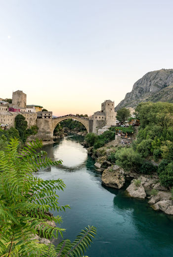 Stari most over river neretva in city against clear sky during sunset