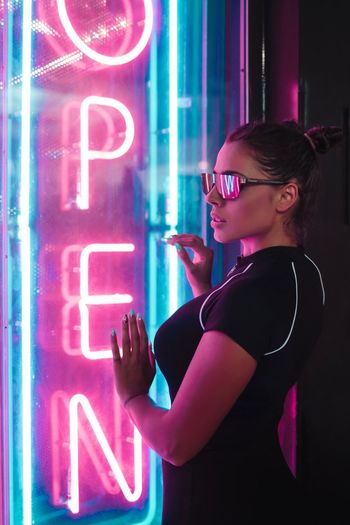Woman standing by illuminated neon sign