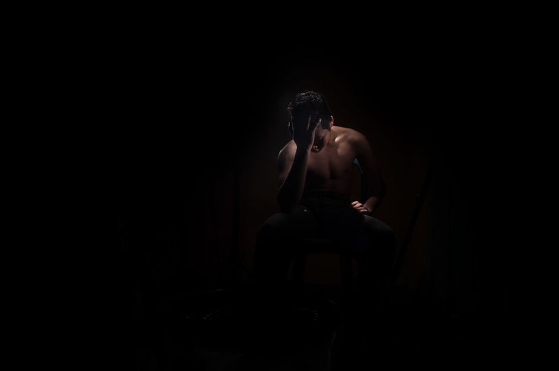 Portrait of shirtless man sitting against black background