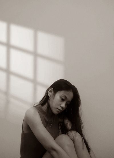 Portrait of young woman sitting against wall at home