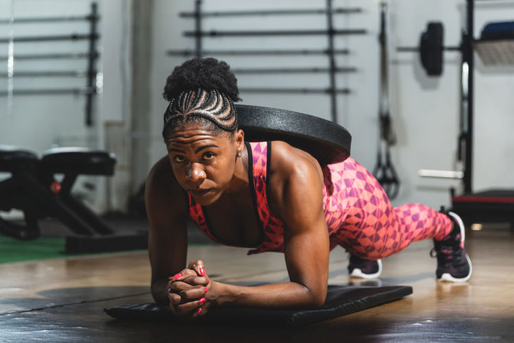 Woman training in modern light studio. doing a plank with weight on your back. flexion on weights.