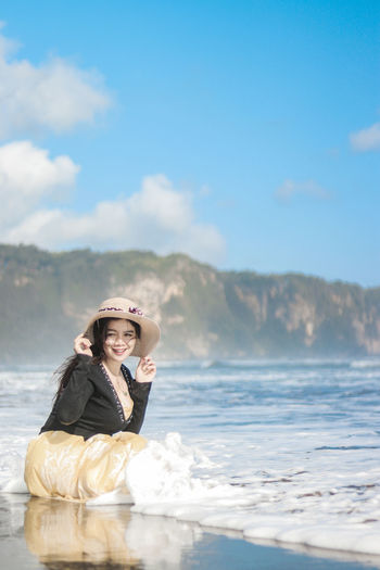 Portrait of woman sitting on beach against sky