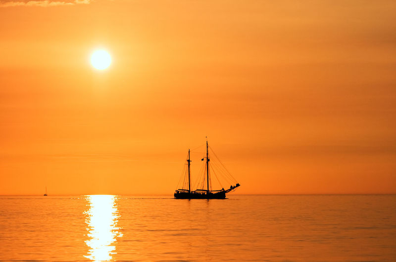 Silhouette sailboat sailing on sea against orange sky