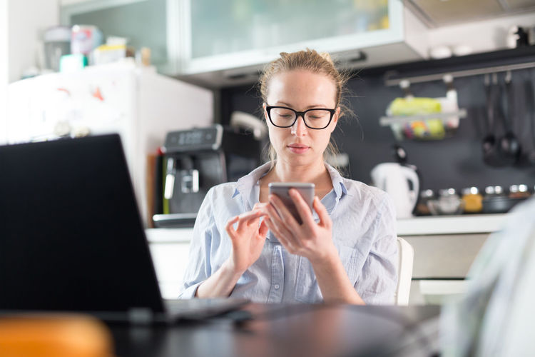 Businesswoman using smart phone sitting at home