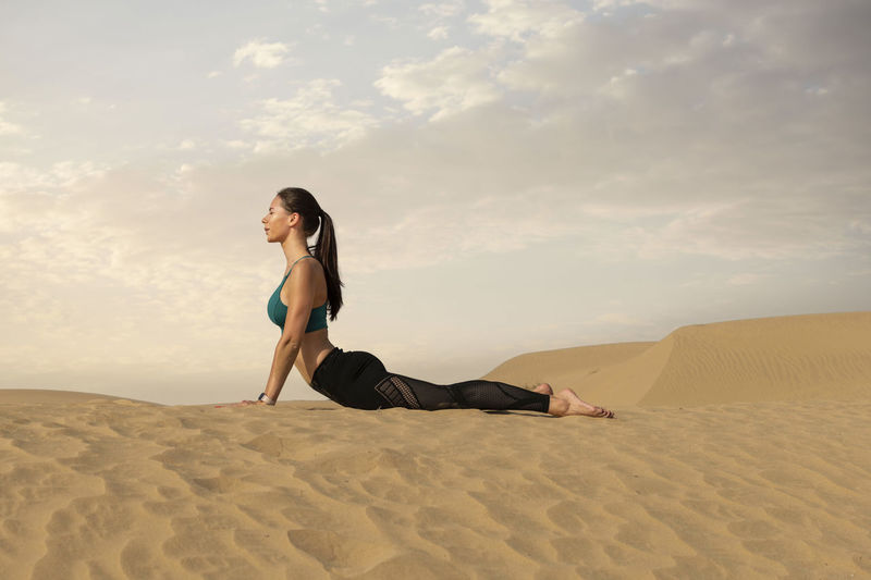 Full length of woman relaxing on sand in desert against sky