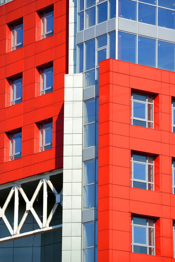 Part of the facade of a modern building with red walls, square windows, the blue mirrored glass. 