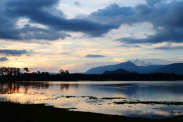 Scenic view of lake by silhouette mountains against sky during sunset
