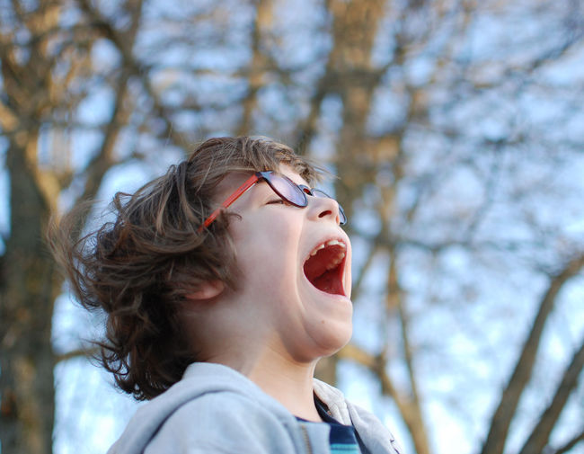 Close-up of boy screaming while standing against bare trees