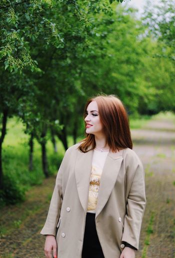 Young woman looking away against tree