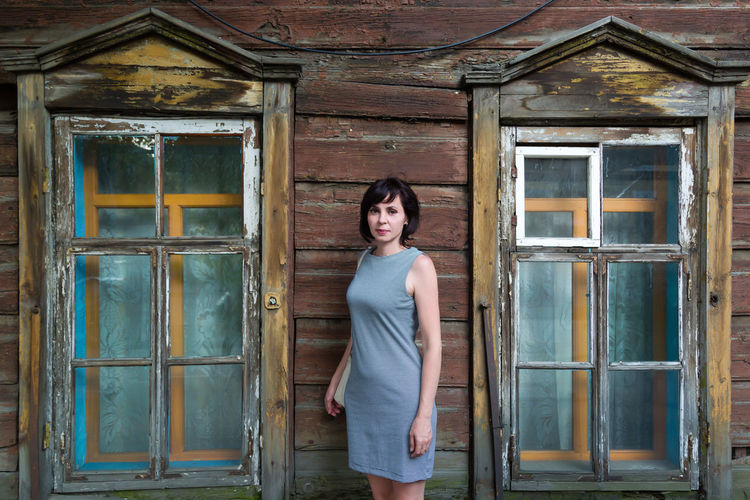 A brunette woman stands in an old wooden abandoned building.
