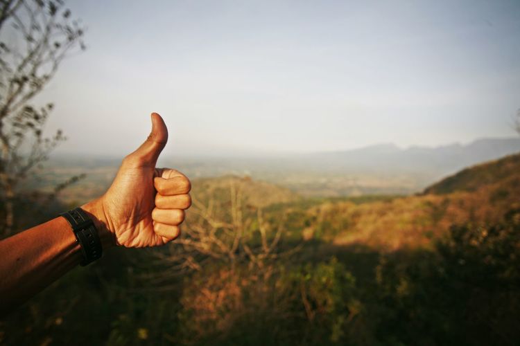 Thumb up midsection of person against sky