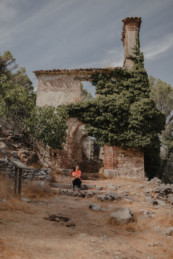Distant female traveler sitting on stone and observing ancient ruined buildings located in highlands while visiting grazalema village in spain during vacation