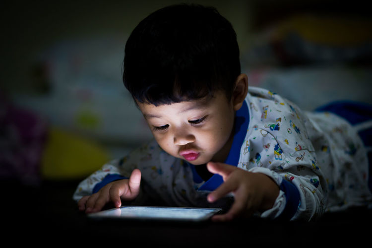 Cute baby boy using digital tablet at home in darkroom