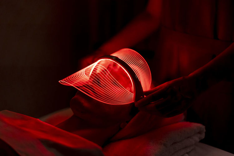 Young woman wearing red mask during rejuvenating treatment at beauty spa