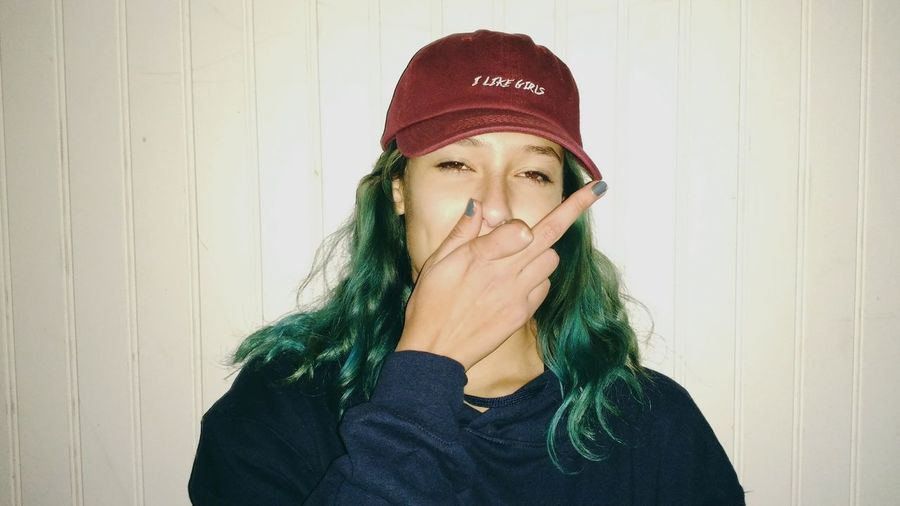 Portrait of woman showing obscene gesture against white wall