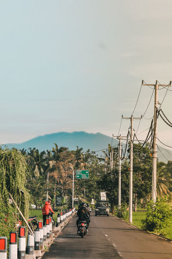 Rear view of people riding motorcycle on road against sky