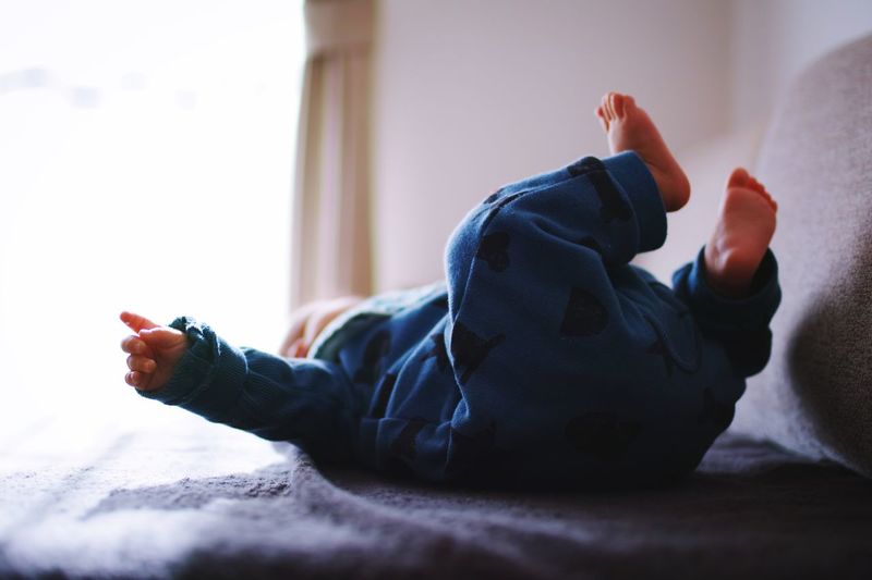 Low section of child lying on bed at home