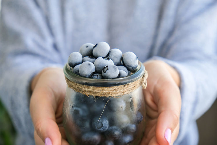 Woman holding bowl with frozen blueberry fruits. harvesting concept. female hands collecting berries