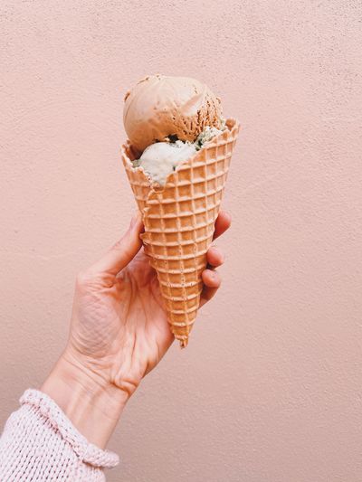 Ice cream cone on pink faded pastel color background. hand holding chocolate ice cream in wafer cup