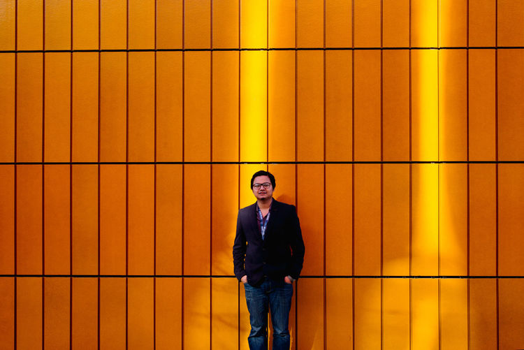 Portrait of a young man standing against yellow wall
