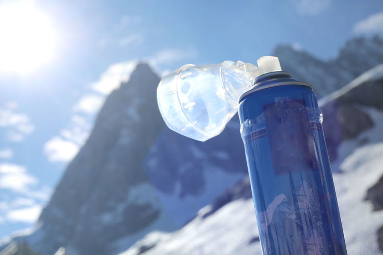 Low angle view of ice bottle against blue sky on sunny day