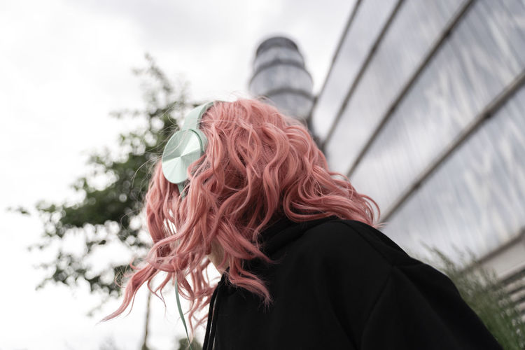 Young woman with pink dyed hair listening music through headphones