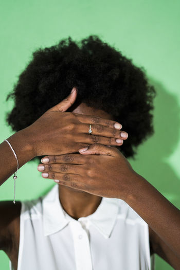 Young woman hiding face with hand while standing against green background