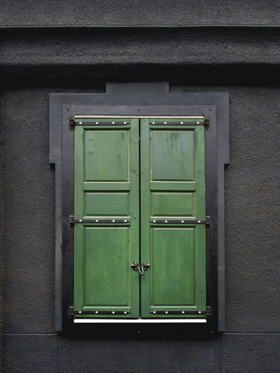 Black wall of building with window locked on wooden green shutters.modern details and vintage style.