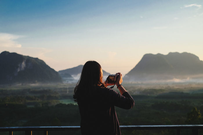 Rear view of woman photographing mountain against sky