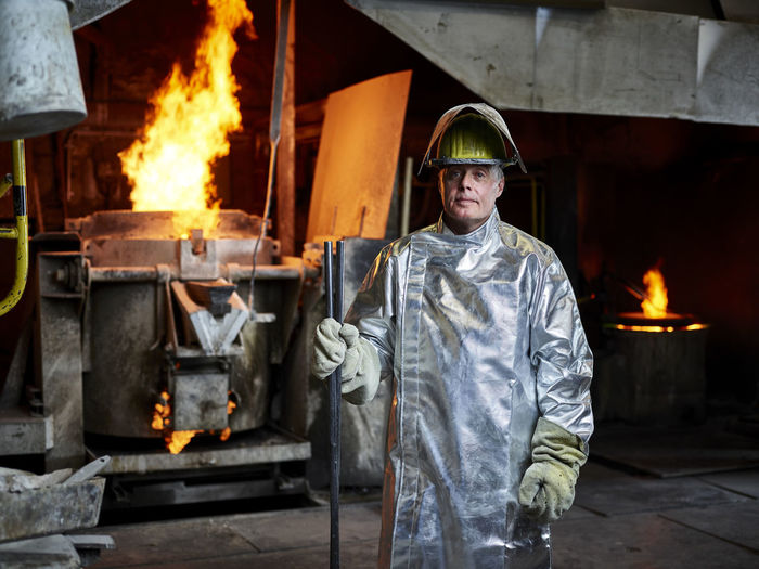 Metal worker wearing protective workwear standing with pipe in industry