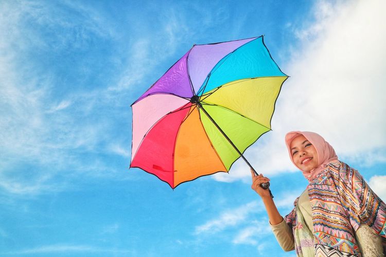 Low angle view of woman holding multi colored umbrella against sky