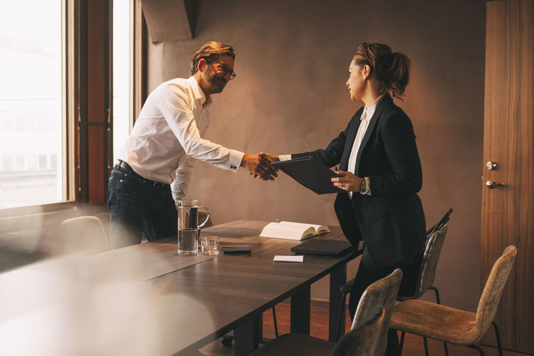 Female lawyer shaking hands with male customer after meeting at table in office