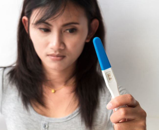 Upset woman holding positive pregnancy test result against wall