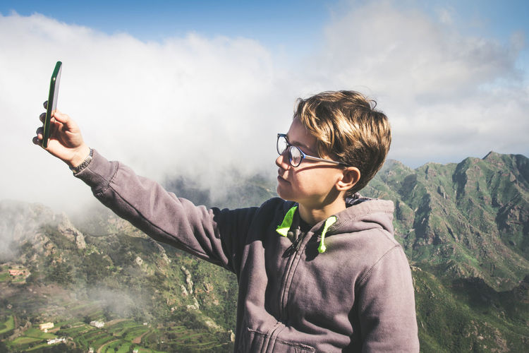 Boy doing selfie while standing against mountain range