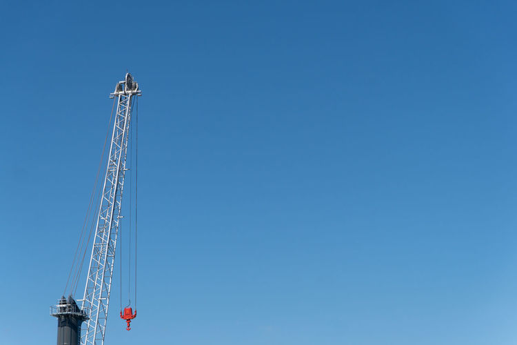 Low angle view of machinery at construction site against clear blue sky