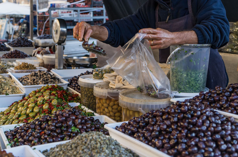 Midsection of vendor packing olives in bag at market stall