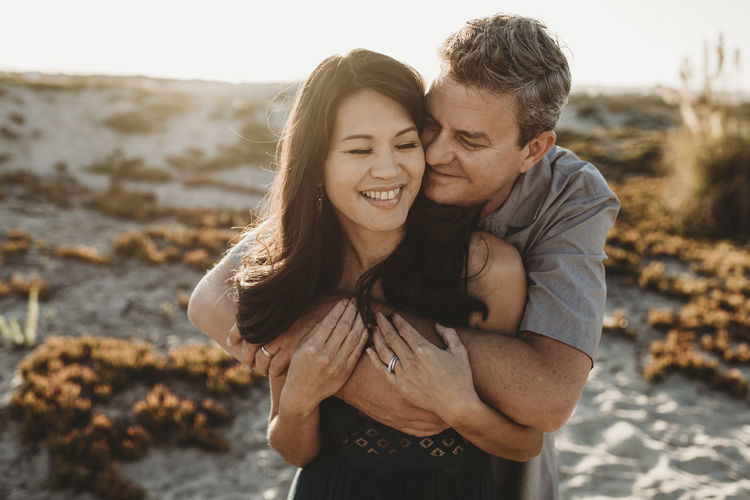 Loving husband with closed eyes embraces beautiful smiling wife