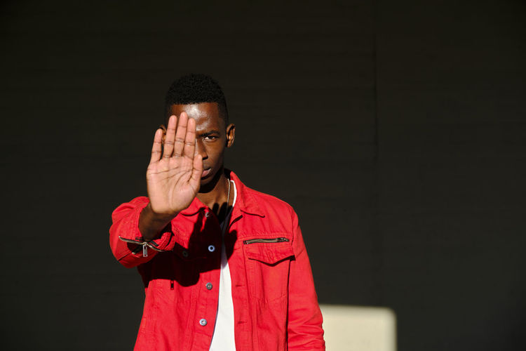 Young man in red jacket making stop gesture in sunlight