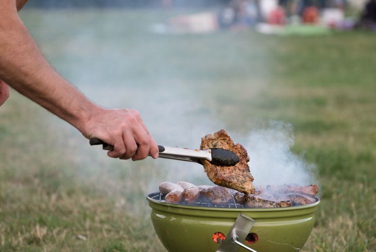 Cropped hand of man cooking food on barbecue at field