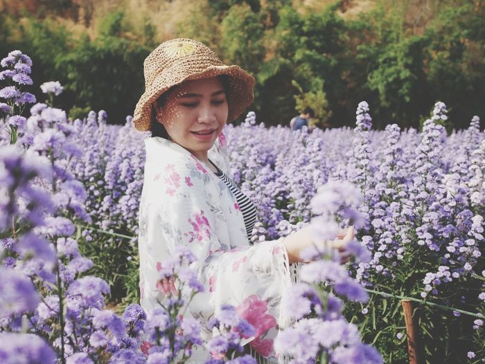 Young woman wearing hat standing amidst flowering plants