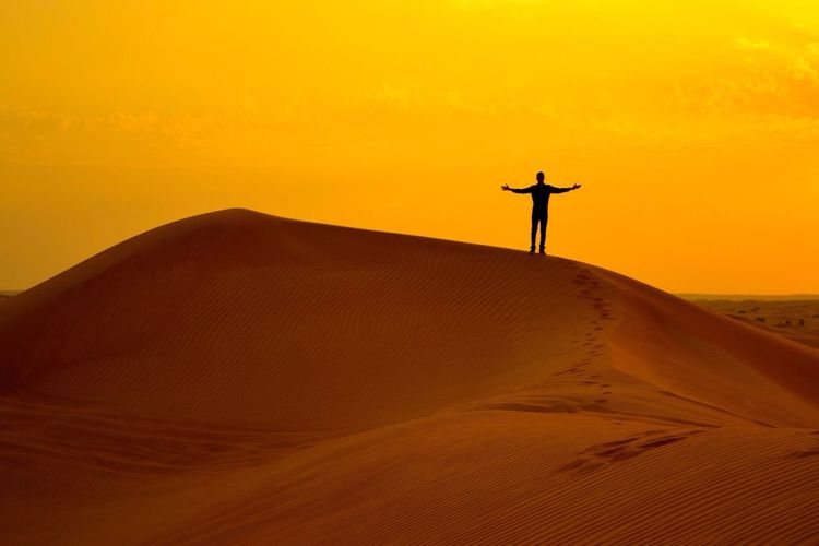 Silhouette man standing on desert against orange sky