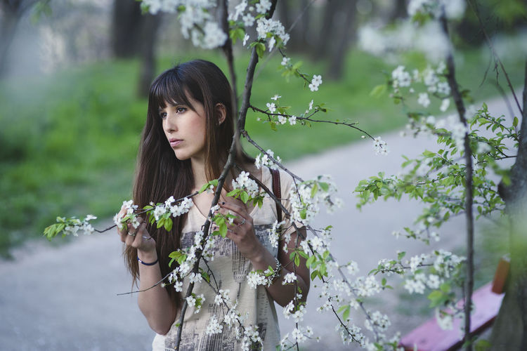 Thoughtful woman amidst flowering tree at park