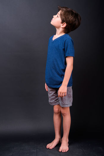 Boy looking away while standing against black background